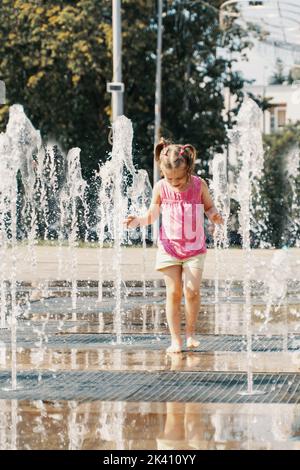 petite fille jouant avec de petites fontaines sur la place urbaine Banque D'Images