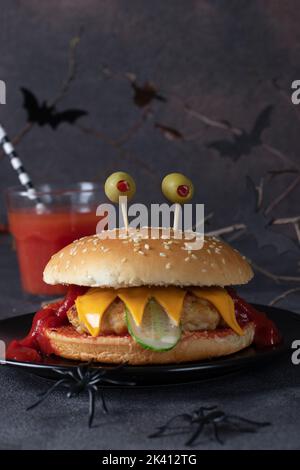 Hamburger de poulet monstre avec toast au fromage, ketchup, olives et concombre sur fond gris. Cuisine créative d'Halloween Banque D'Images