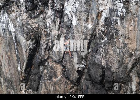 Sagres, Portugal - 30 mai 2022 : grimpeur de roche femelle unique montant une falaise côtière rugueuse fixée avec une corde supérieure en été près de Sagres Portugal Banque D'Images