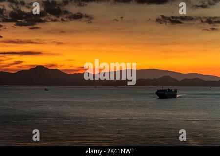 Un petit cargo navigue au large de la côte au coucher du soleil Banque D'Images