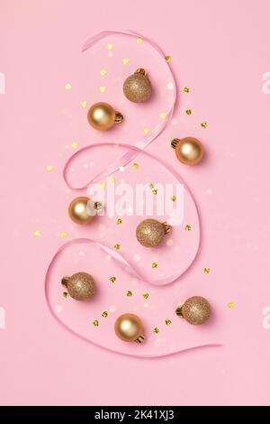 Carte de Noël avec boules dorées à paillettes, confetti en forme de coeur et ruban de satin sur fond rose avec lumières floues bokeh Banque D'Images