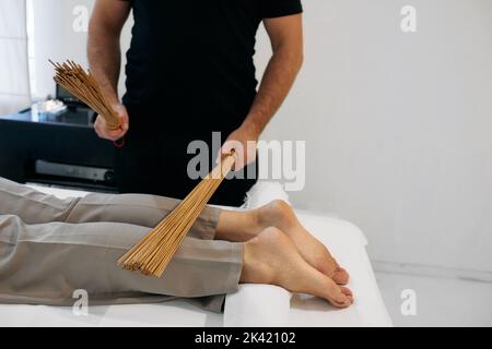 Balais en bambou dans les mains du masseur en mouvement tout en massant les jambes du patient du salon de massage. Massage avec des bâtonnets de bambou Banque D'Images