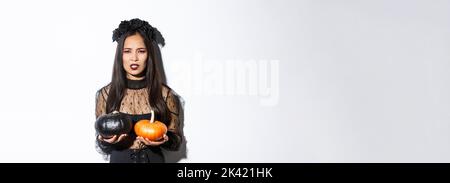 Image de sorcière en colère grimacing jetant des citrouilles, fille célébrant halloween, debout sur fond blanc Banque D'Images