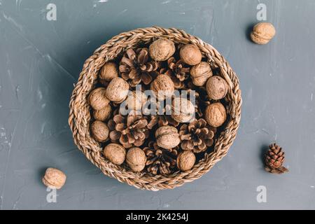Noix crues en carapace et cônes de pin en panier comme décoration de table d'automne ou de Noël sur fond gris foncé.Vue de dessus, espace de copie Banque D'Images