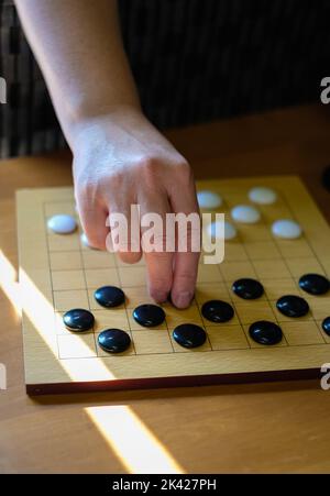 Plateau de jeu Chinese Go, vue rapprochée des pièces de pierre noir et blanc, AlphaGo. Mains d'une femme jouant à un jeu de société asiatique. Mise au point sélective Banque D'Images