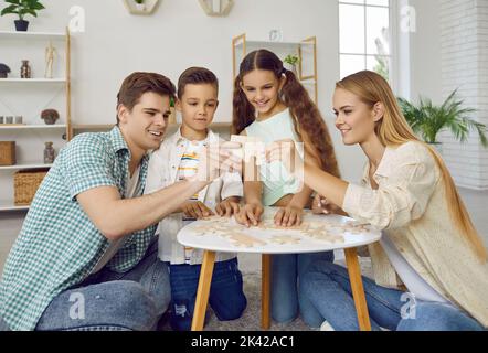 Une famille amicale avec deux enfants joue à des puzzles à la table assise sur le sol à la maison le week-end. Banque D'Images