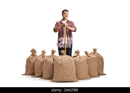 Portrait complet d'un fermier mâle avec une pelle debout derrière des sacs de toile de jute isolés sur un fond blanc Banque D'Images