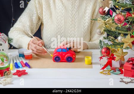 Instructions étape par étape pour la photo d'un décor de Noël - une fille peint une voiture en plâtre, étape 6 - colorant les phares avec de la peinture jaune Banque D'Images