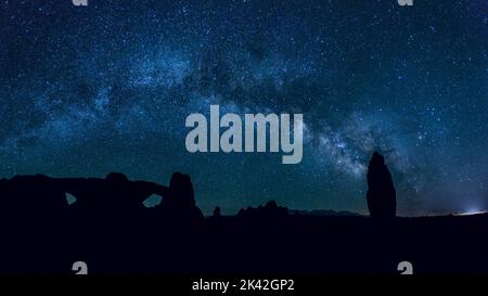 Milky Way Galaxy au-dessus des silhouettes d'une flèche de grès et des fenêtres nord et sud dans le parc national d'Arches, Moab, Utah. Banque D'Images