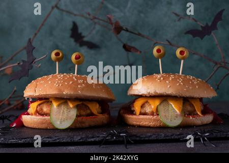 Deux burgers de poulet monstre drôle avec toasts au fromage, ketchup, concombre et yeux d'olive. Cuisine créative d'Halloween Banque D'Images