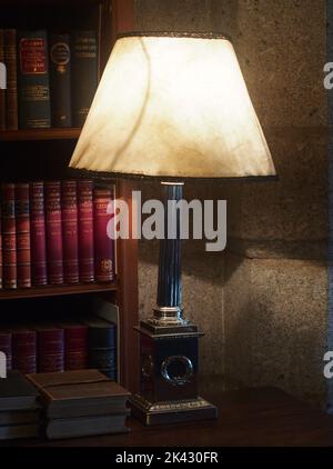 Une grande lampe de table à base lourde, qui illumine une bibliothèque de livres, des volumes dans son éclat Banque D'Images