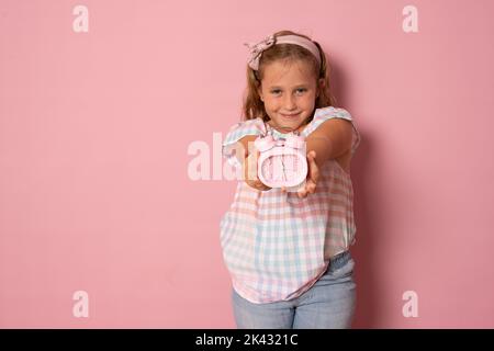 Concept enfants. Une fille tient un réveil dans ses mains, joue avec elle, regarde la caméra. Isolé sur fond blanc. Banque D'Images