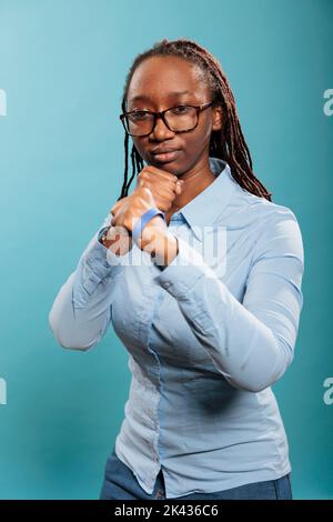 Les jeunes adultes défensifs en auto-défense se posent lorsqu'ils rencontrent une menace de vie. Femme sérieuse et courageuse se prépare à la boxe tout en affrontant les poings avec force sur fond bleu Banque D'Images