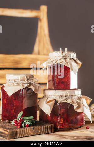 Pots de confiture de mûres et de poires maison avec papier artisanal sur les couvercles sur la surface en bois, à côté des baies de lingonis fraîches. Verticale Banque D'Images