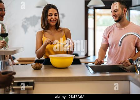 une femme latine prépare une salade tout en riant avec deux amis Banque D'Images