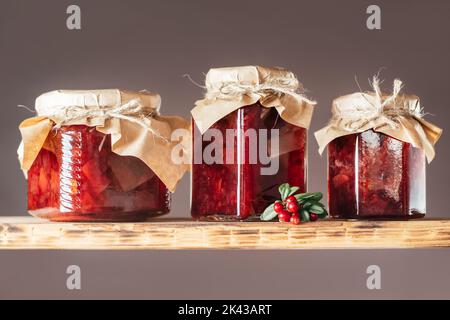 Pots de confiture de mûres et de poires maison avec papier artisanal sur les couvercles sur une étagère en bois à côté de baies fraîches sur fond brun Banque D'Images