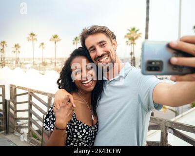 Un jeune couple multiethnique souriant prend un selfie lors de vacances tropicales. Banque D'Images