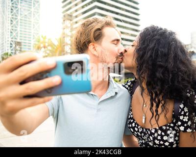 Divers couple hétérosexuel dans l'amour embrassant tout en prenant un selfie. Amoureux, lune de miel Banque D'Images