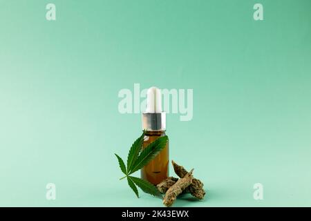 Image d'une bouteille d'huile de cbd et de feuilles de marihuana séchée sur une surface verte Banque D'Images
