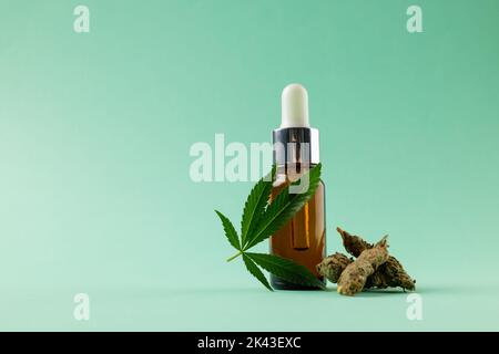 Image d'une bouteille d'huile de cbd et de feuilles de marihuana séchée sur une surface verte Banque D'Images