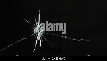 Gros plan d'un panneau de verre cassé et fissuré avec trou rond, sur fond noir avec espace de copie Banque D'Images