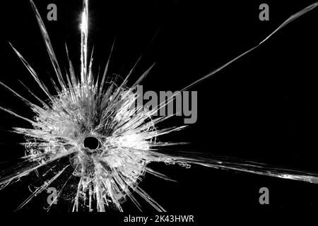 Gros plan d'un panneau de verre cassé et fissuré avec trou rond, sur fond noir avec espace de copie Banque D'Images