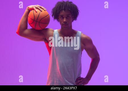 Image d'un joueur de basket-ball biracial avec basket-ball sur fond violet fluo Banque D'Images