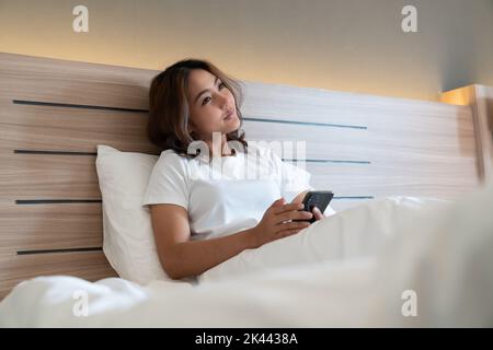 Les jeunes femmes asiatiques qui se coutent au lit envoient des SMS et vérifient les applications sociales sur leur smartphone avant de dormir la nuit. Concept Mobile addict. Banque D'Images