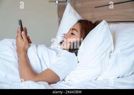 Les jeunes femmes asiatiques qui se coutent au lit envoient des SMS et vérifient les applications sociales sur leur smartphone avant de dormir la nuit. Concept Mobile addict. Banque D'Images