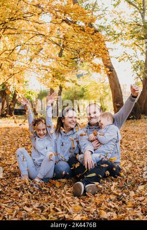 Une famille heureuse et longue qui lante des feuilles d'automne dans le parc à l'automne. Le mode de vie des gens. Parent, enfant. Bonne famille à l'extérieur. Famille amusante. Bonne famille Banque D'Images