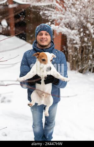 Un homme tient un chien de race Jack russell terrier et le jette dans la neige en hiver. Photo verticale. Banque D'Images