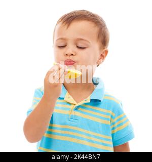 Inculquer de bonnes habitudes alimentaires. Un jeune garçon mignon mangeant une tranche d'orange isolée sur blanc. Banque D'Images