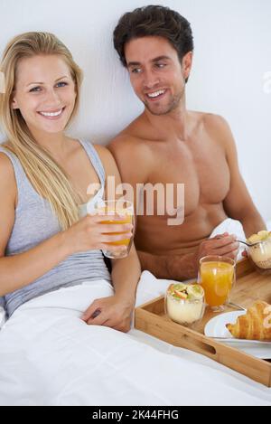 Elle aime les samedis lents. Un jeune couple heureux prenant le petit déjeuner au lit. Banque D'Images