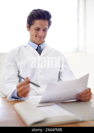 Ces résultats sont prometteurs... un jeune médecin souriant assis à son bureau, qui se charge de la paperasse. Banque D'Images