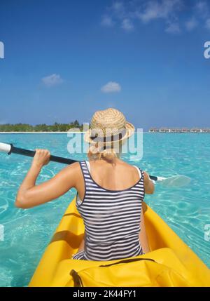 Pagayer au paradis. Une belle jeune femme pagayant sur un bateau dans un océan tropical. Banque D'Images