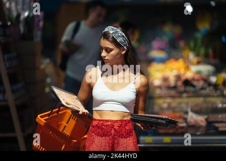 Une jeune femme choisit de la viande dans une épicerie Banque D'Images