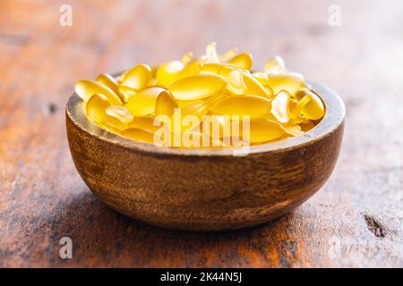 Capsules d'huile de poisson dans un bol. Pilules jaunes omega 3 sur la table en bois. Banque D'Images
