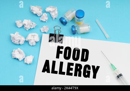 Concept de médecine. Sur fond bleu, une seringue, un médicament, des morceaux de papier blanc froissé et une feuille avec l'inscription - ALLERGIE ALIMENTAIRE Banque D'Images