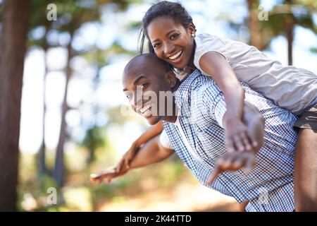 Toujours ludique et affectueux. Portrait d'un mari portant sa femme sur le dos tout en appréciant une journée dehors. Banque D'Images