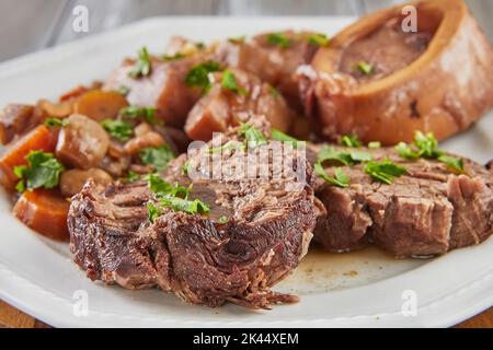 Ossobuco avec légumes sur plaque avec couteau et fourchette sur fond de bois Banque D'Images