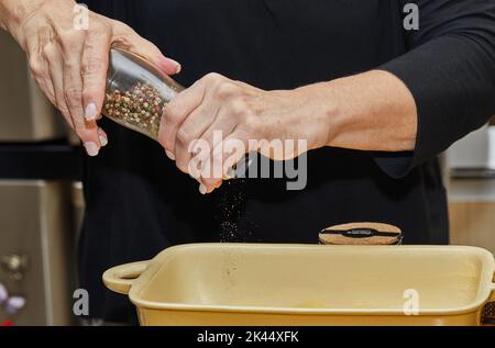 Recette de gratin de pommes de terre étape par étape. Les mains poivrer des tranches de pommes de terre dans un plat à pâtisserie en verre. Casserole de pommes de terre Banque D'Images