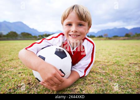 Attente du début de la pratique. Portrait d'un jeune garçon allongé sur un terrain de football. Banque D'Images