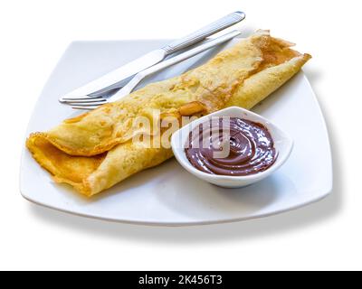 Crêpe pliée avec du chocolat sur le côté sur une assiette blanche avec de l'argenterie. Banque D'Images