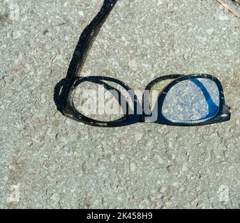 Un gros plan d'une paire de lunettes brisées éraflées sur le sol Banque D'Images