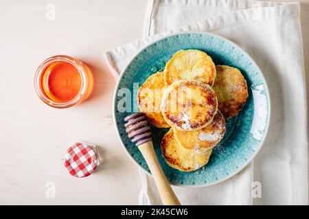 Crêpes au fromage cottage servies avec du miel sur une assiette bleue. Banque D'Images
