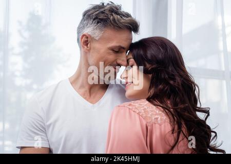 Femme souriante en robe de satin debout près de mari à la maison, image de stock Banque D'Images