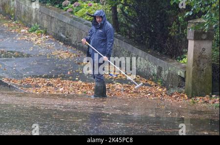 Un homme tente de soulager les inondations en éliminant les débris automnaux des drains lors de fortes pluies à Glasgow. Date de la photo: Vendredi 30 septembre 2022. Banque D'Images