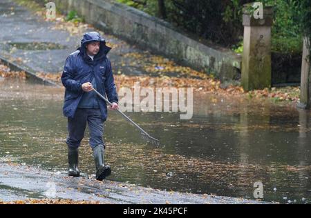 Un homme tente de soulager les inondations en éliminant les débris automnaux des drains lors de fortes pluies à Glasgow. Date de la photo: Vendredi 30 septembre 2022. Banque D'Images