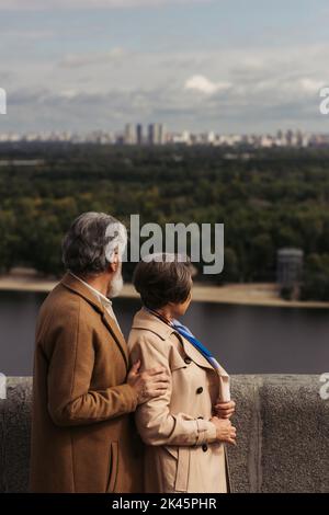 vue arrière d'un couple senior en couches beige debout sur le pont près de la rivière, image de stock Banque D'Images