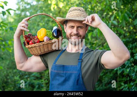 un homme heureux en chapeau de paille tient le panier rempli de légumes Banque D'Images